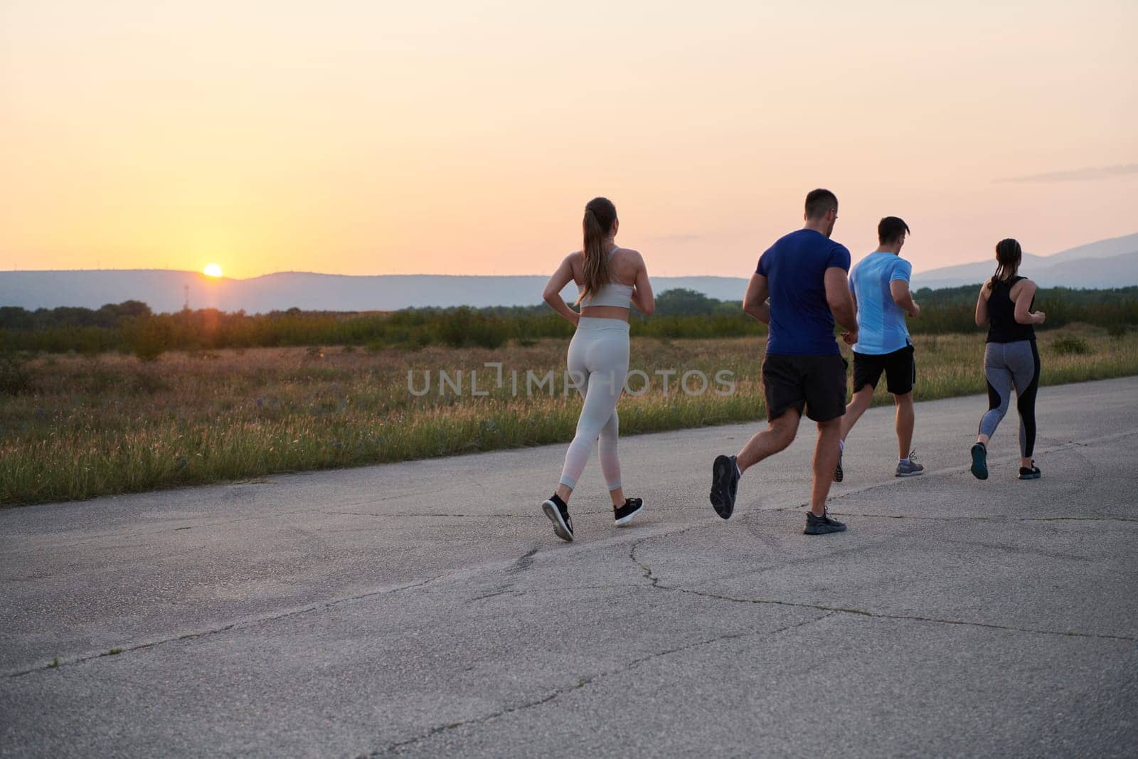 A diverse group of runners finds motivation and inspiration in each other as they train together for an upcoming competition, set against a breathtaking sunset backdrop.