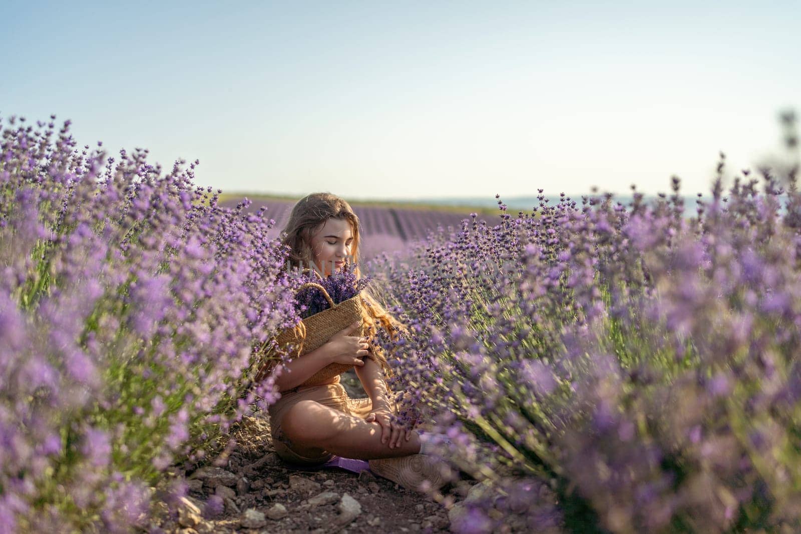 Girl is sitting in a field of purple flowers. She is holding a basket of flowers and smiling. Scene is peaceful and serene, as the girl is surrounded by the beauty of nature