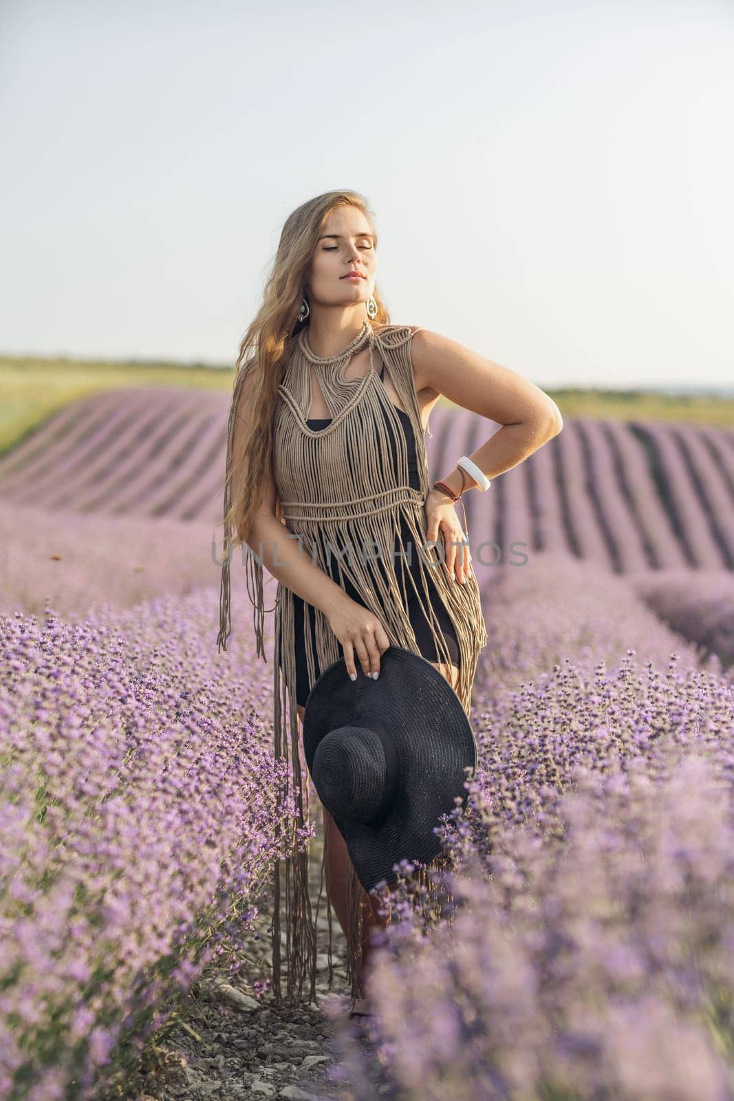 A woman is standing in a field of purple flowers, wearing a black dress and a black hat. by Matiunina