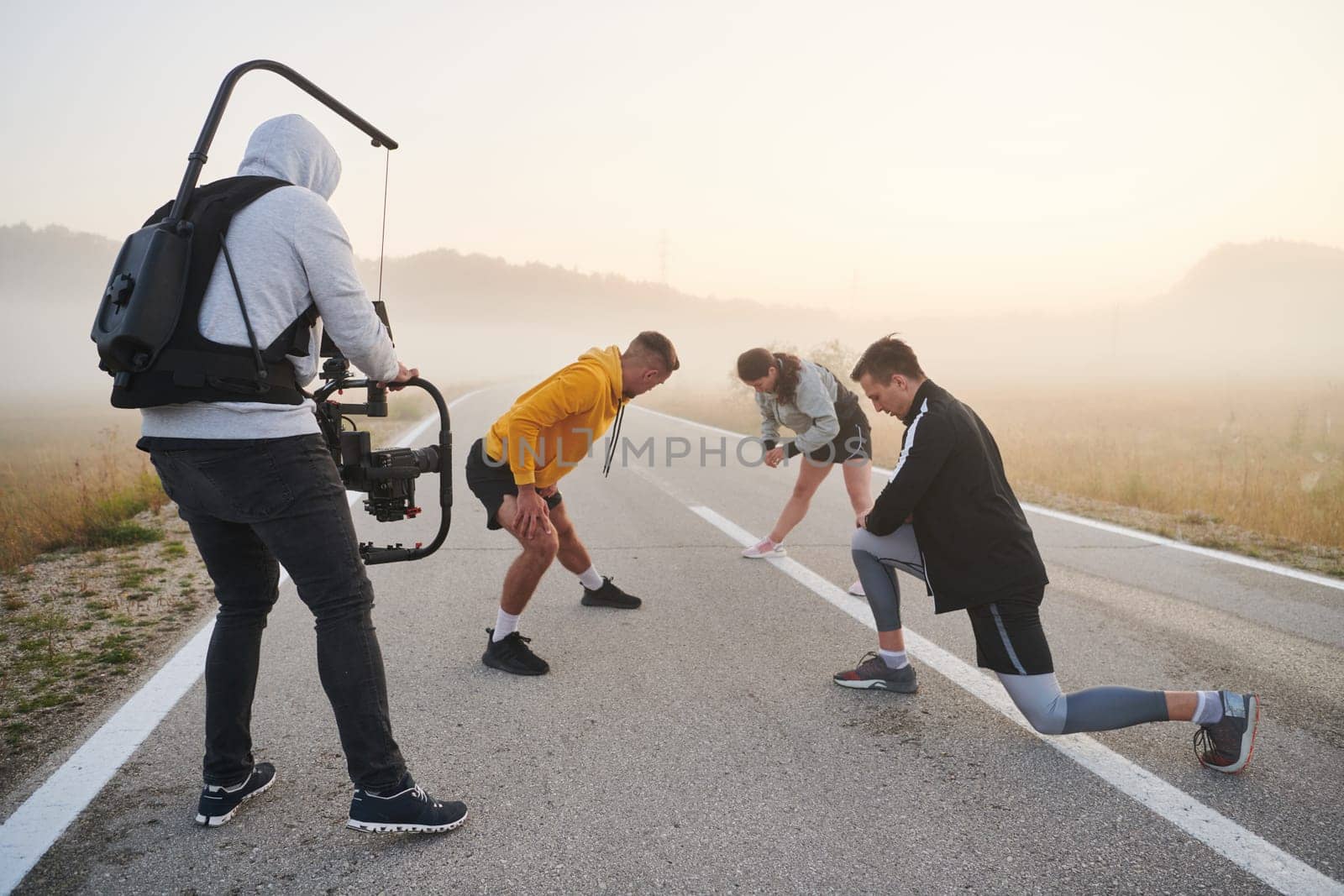 A skilled videographer captures the dynamic scene as athletes engage in warming up and stretching exercises in preparation for their morning run, showcasing dedication and teamwork behind the lens.