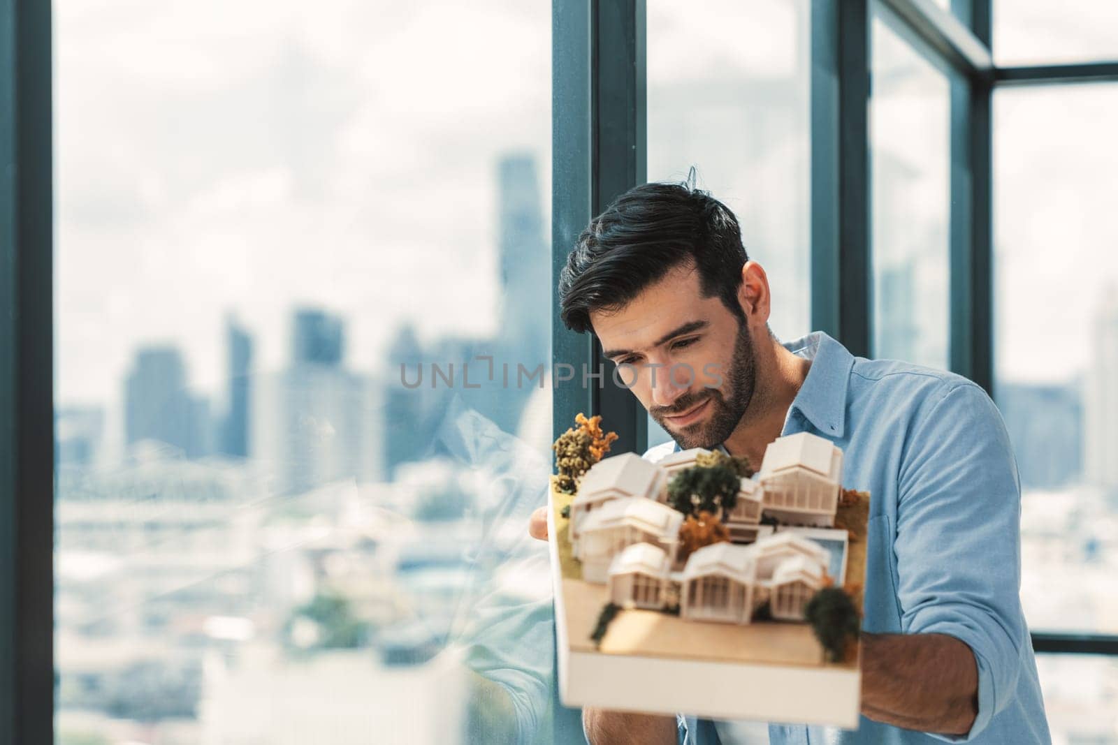 Businessman in casual outfit holding house model while checking house construction. Architect engineer inspect building model while standing near window with skyscraper. Civil engineering. Tracery.