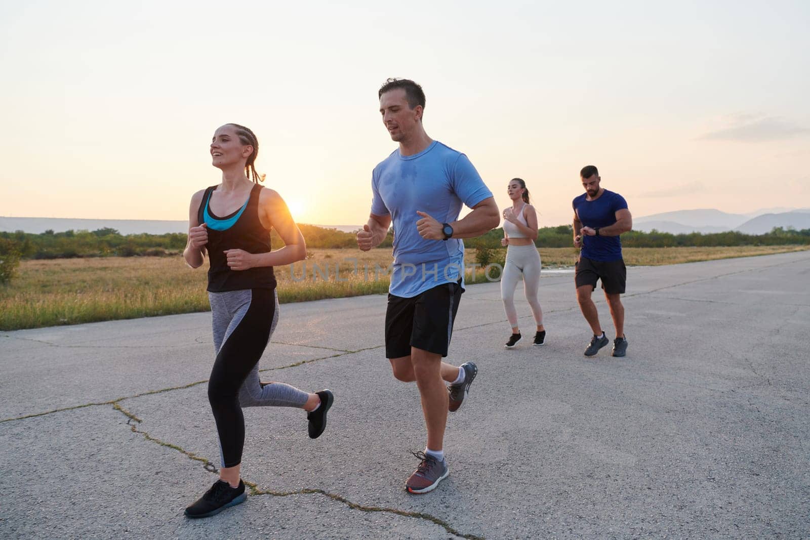 A diverse group of runners finds motivation and inspiration in each other as they train together for an upcoming competition, set against a breathtaking sunset backdrop.