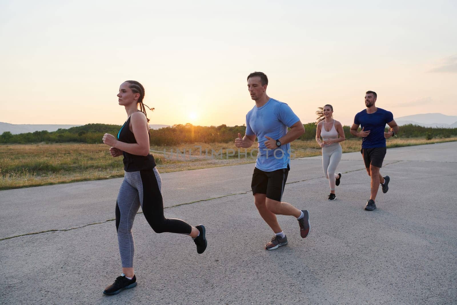 A diverse group of runners finds motivation and inspiration in each other as they train together for an upcoming competition, set against a breathtaking sunset backdrop.