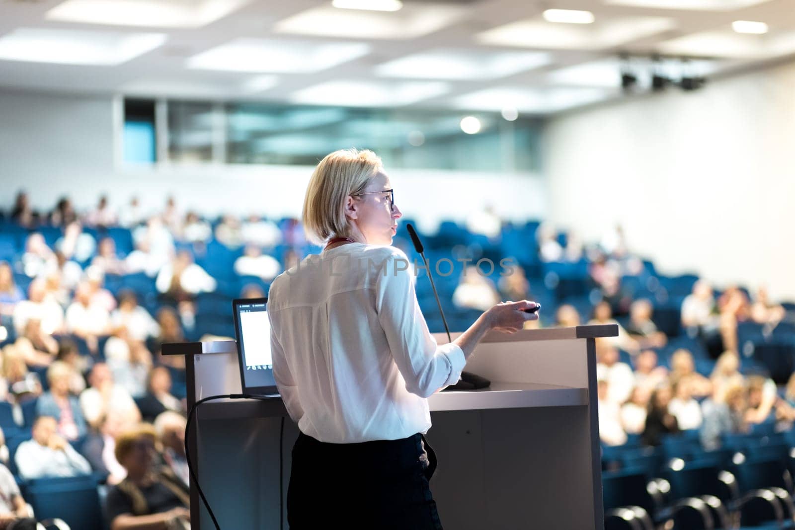 Female speaker giving a talk on corporate business conference. Unrecognizable people in audience at conference hall. Business and Entrepreneurship event