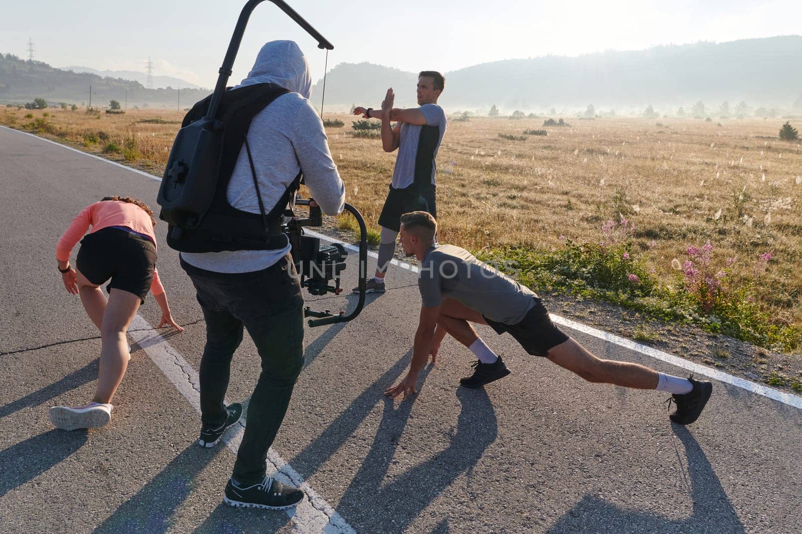 A skilled videographer captures the dynamic scene as athletes engage in warming up and stretching exercises in preparation for their morning run, showcasing dedication and teamwork behind the lens.