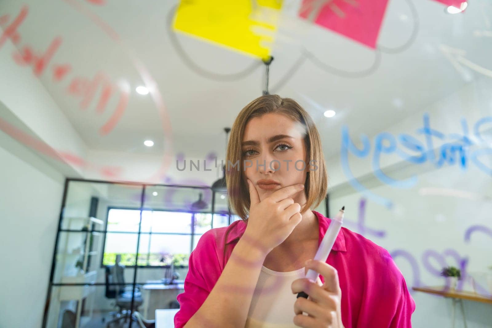 Portrait of young caucasian businesswoman thinking with confused face expression while standing in front of glass board with sticky notes and mind map at creative business meeting. Immaculate.