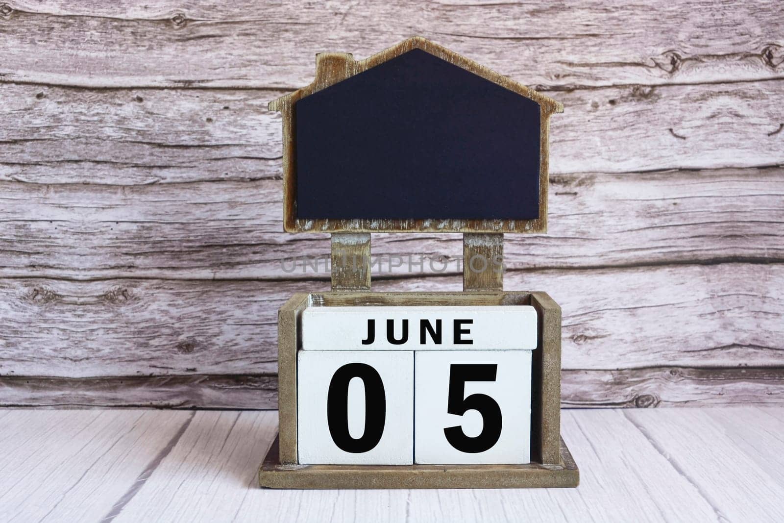 Chalkboard with June 05 date on white cube block on wooden table. by JennMiranda