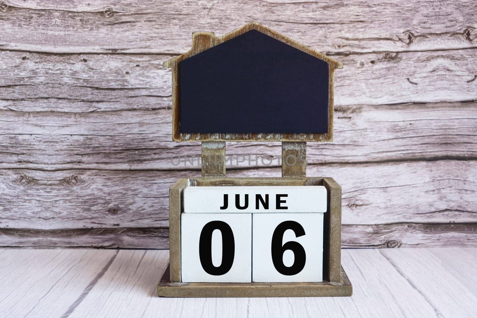 Chalkboard with June 06 date on white cube block on wooden table. by JennMiranda