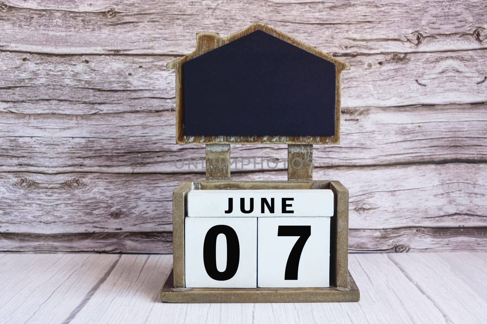 Chalkboard with June 07 calendar date on white cube block on wooden table.