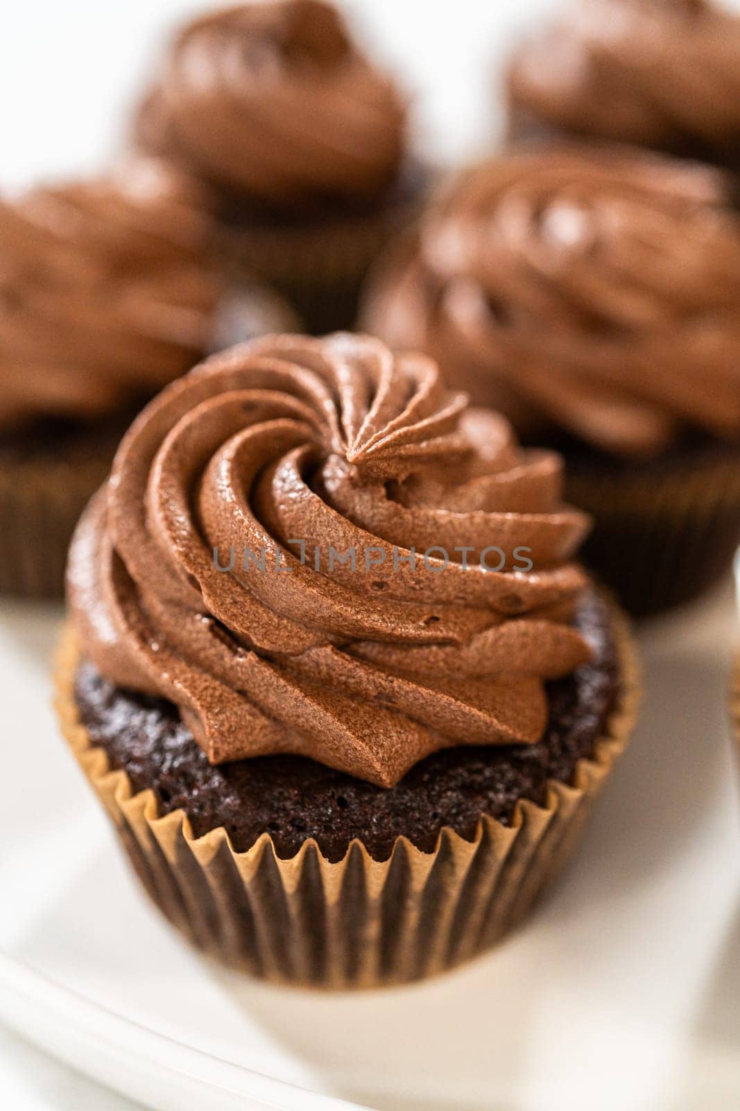 Freshly baked cupcakes have been masterfully infused with rich caramel and adorned with velvety chocolate frosting, all elegantly presented on a pristine white serving plate.