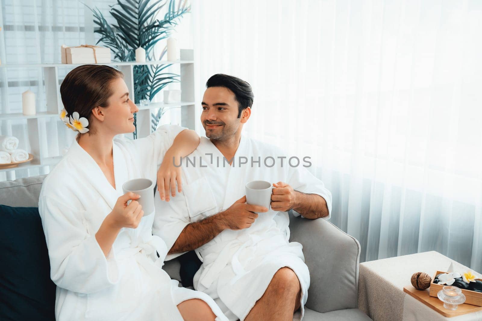 Beauty or body treatment spa salon vacation lifestyle concept with couple wearing bathrobe relaxing with drinks in luxurious hotel spa or resort room. Vacation and leisure relaxation. Quiescent