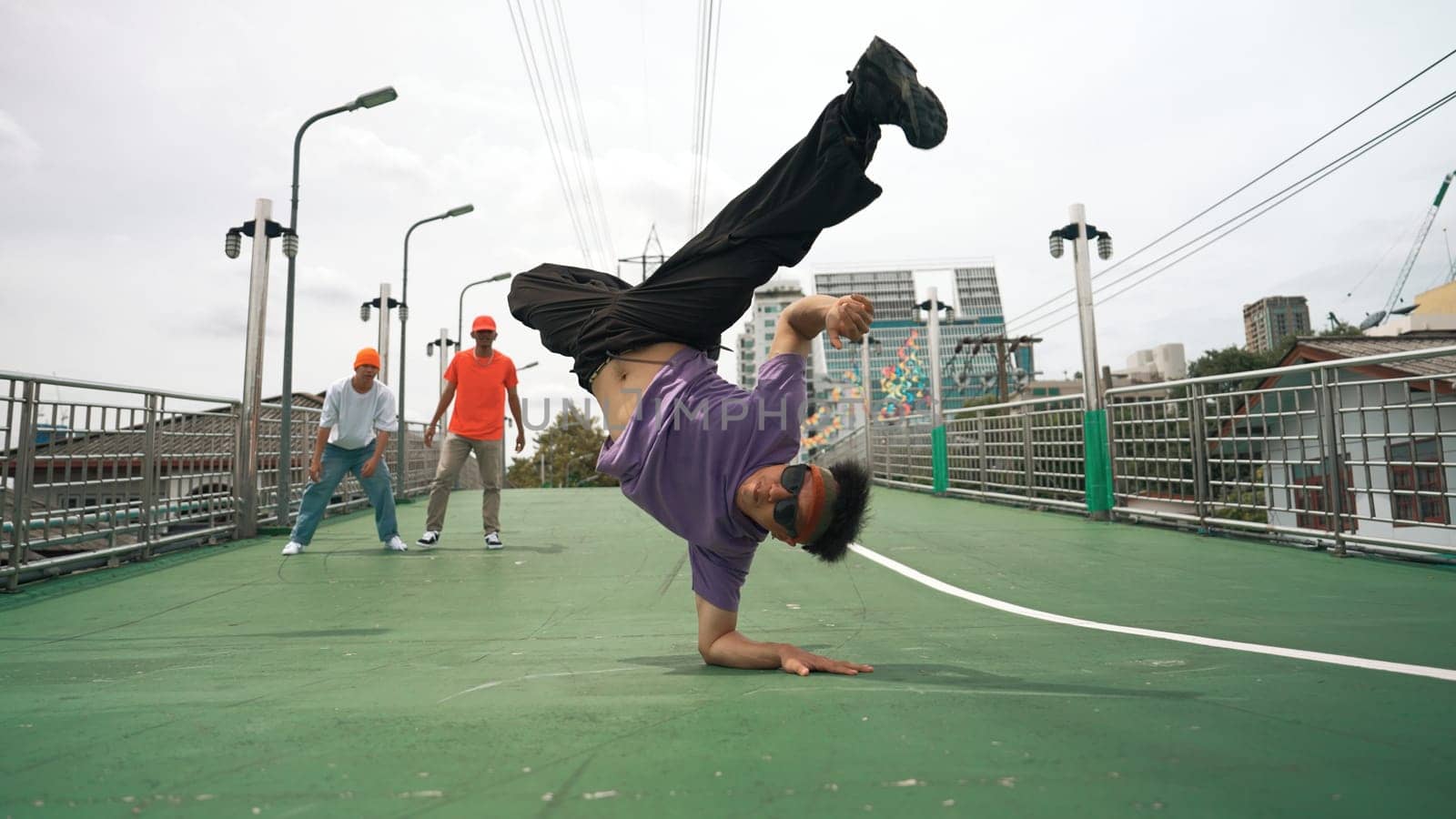 Low angle camera of hipster doing freeze pose while looking at camera. Group of break dancer looking and cheering happy man practice break dancing. Modern lifestyle. Outdoor sport 2024. Sprightly.