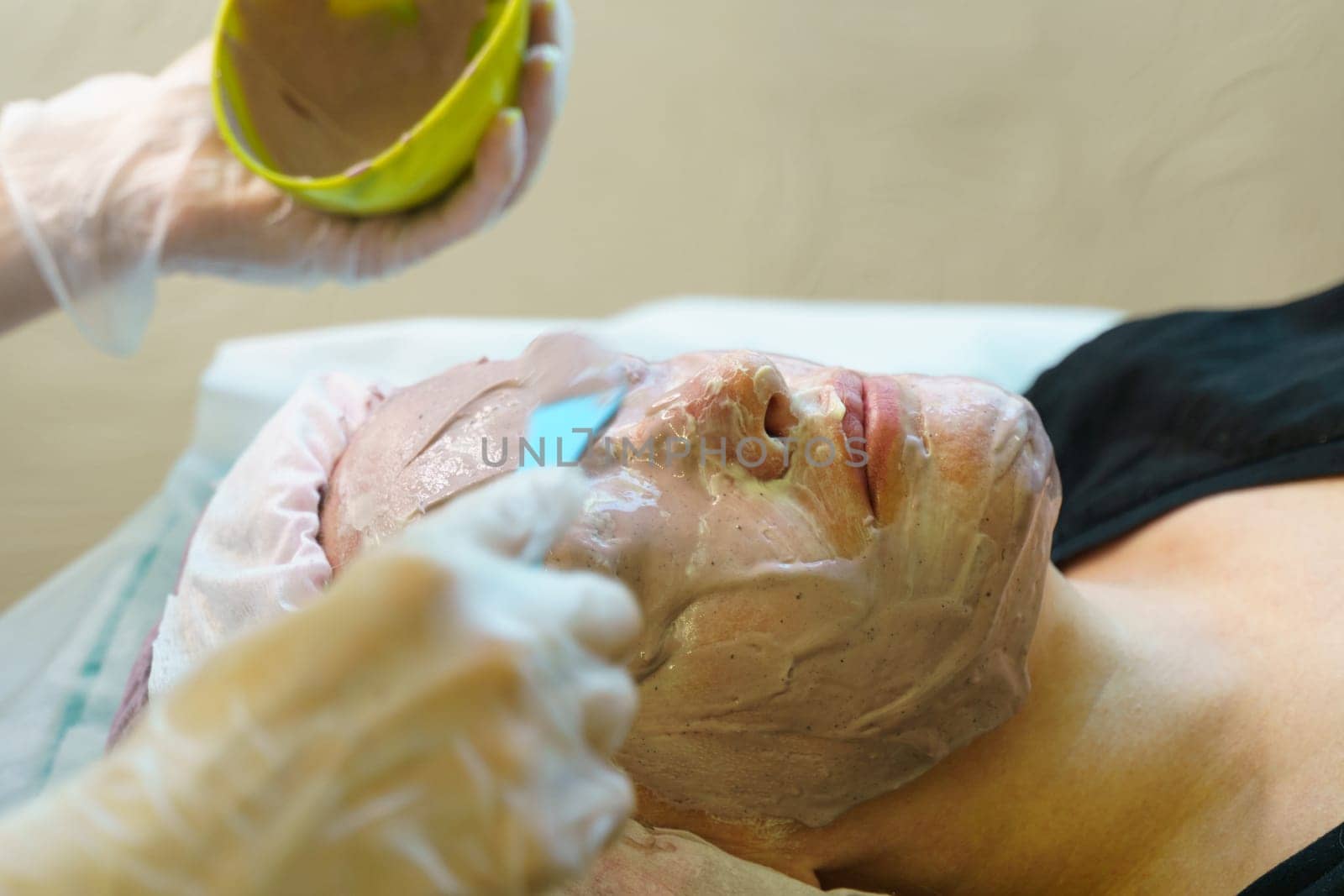 A woman is having a facial mask applied to her face by a skincare professional in a spa setting.