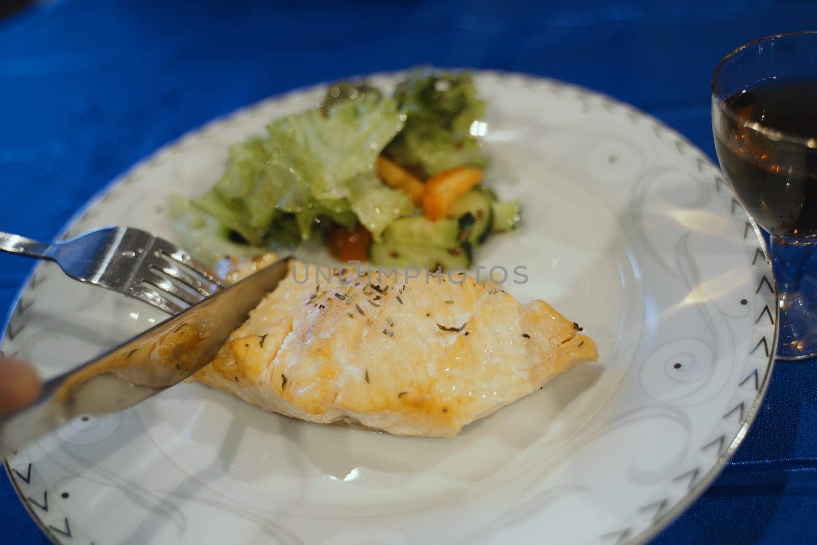 A piece of grilled salmon seasoned with herbs on a white plate accompanied by a fresh green salad, ready for a healthy meal.