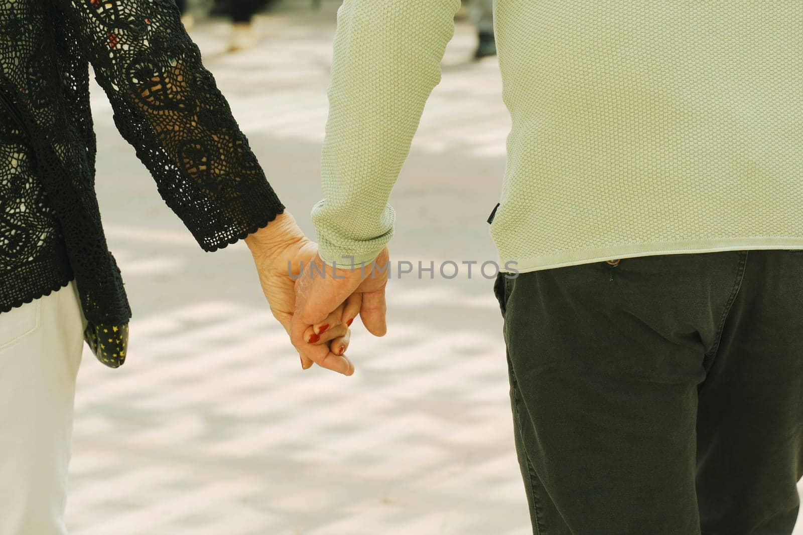 Two individuals walking hand in hand, strolling down a city street with buildings in the background.