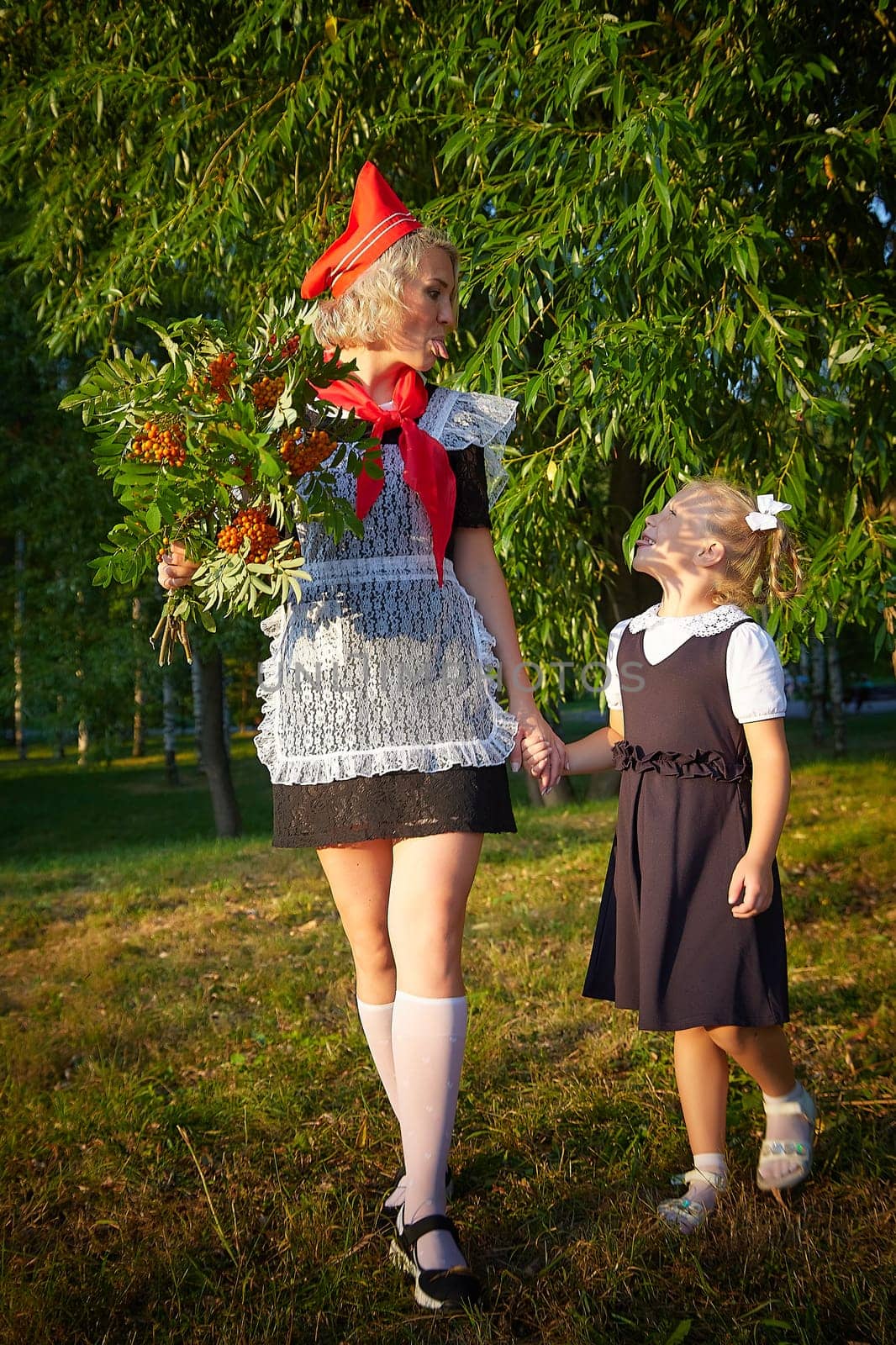 Young and adult schoolgirl on September 1 with flowers. Generations of schoolchildren of USSR and Russia. Female pioneer in red tie and October girl in modern uniform. Mother and daughter having fun by keleny