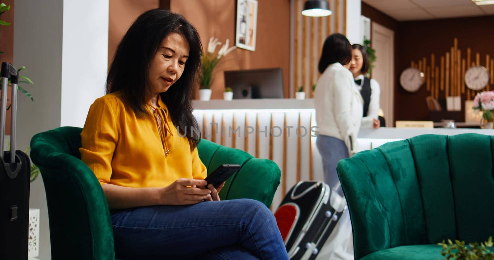 Traveler searching landmarks and places to visit during her stay, using smartphone and relaxing in lounge area at hotel. Asian woman creating a plan for the vacation, waiting to confirm booking.