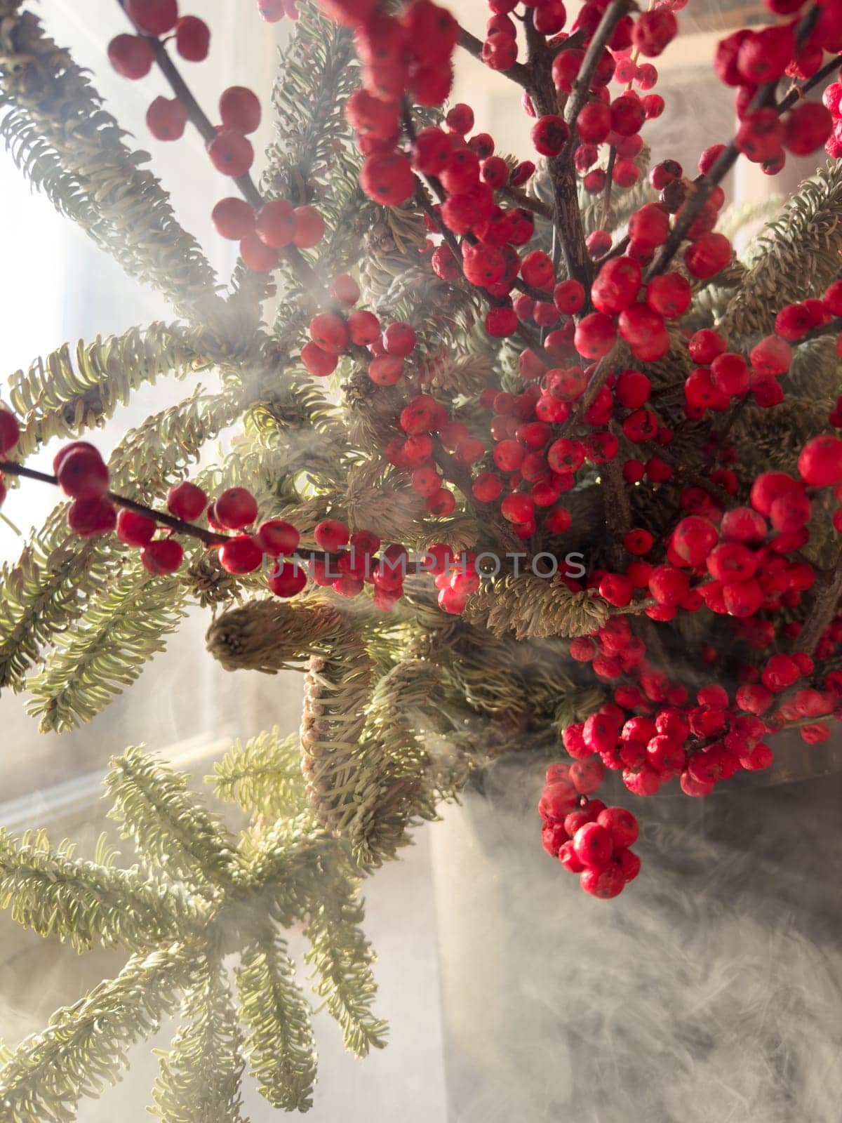 a bouquet of branches with red berries and fir branches in smoke in sunny weather, the rays of the sun through the branches. High quality photo