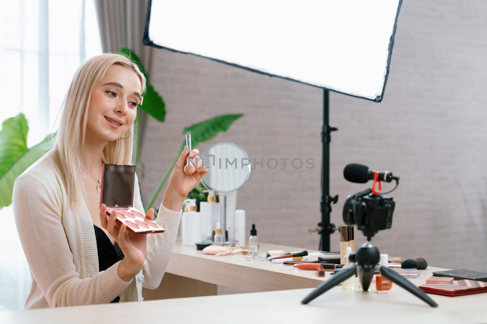 Young woman making beauty and cosmetic tutorial video content for social media. Beauty blogger smiles to camera while showing how to beauty care to audience or followers. Blithe