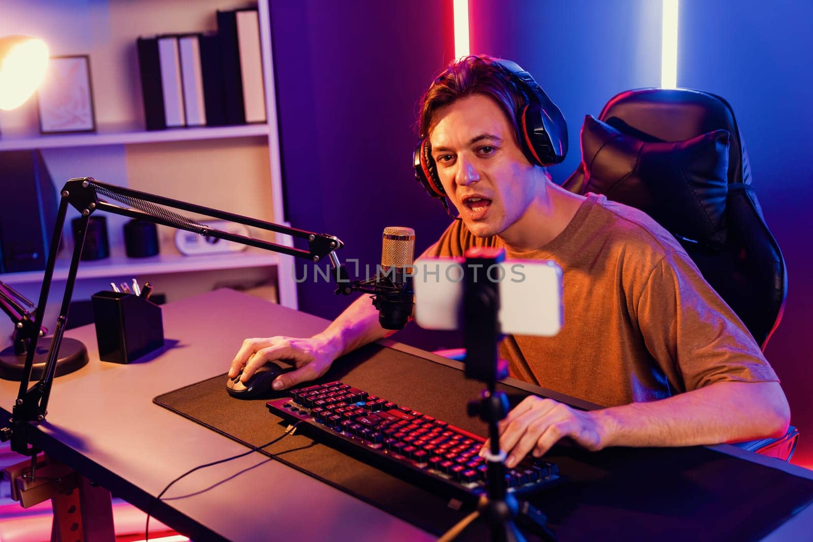 Host channel of gaming smart streamer playing online game, wearing headphone with viewers live steaming on media social online by smartphone talking with team player at neon lighting room. Pecuniary.