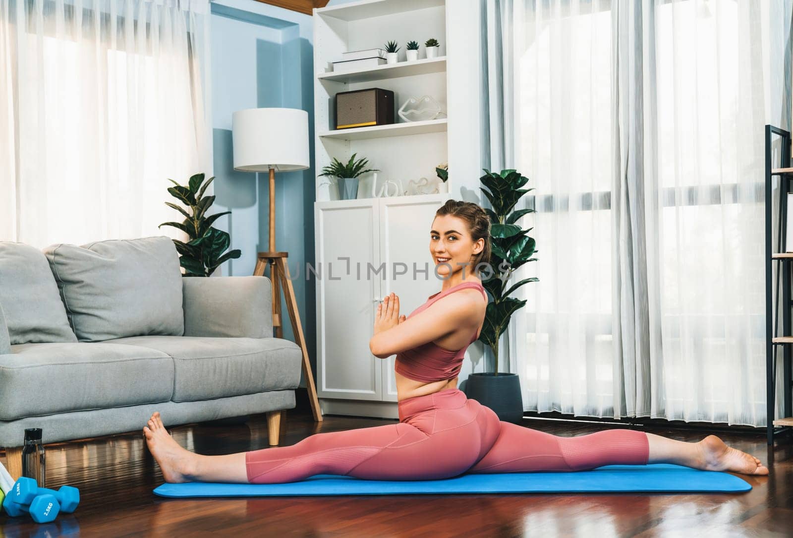 Flexible and dexterity woman in sportswear doing yoga position in meditation posture on exercising mat at home. Healthy gaiety home yoga lifestyle with peaceful mind and serenity.