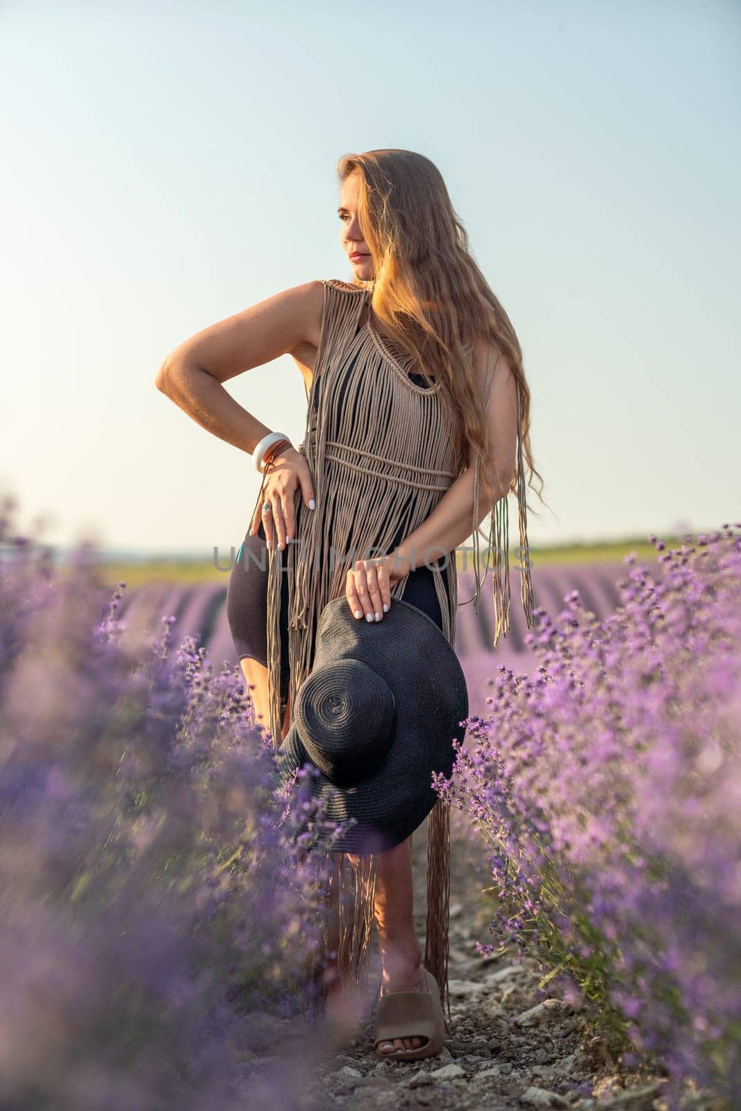 A woman is standing in a field of purple flowers, wearing a black dress and a black hat. by Matiunina