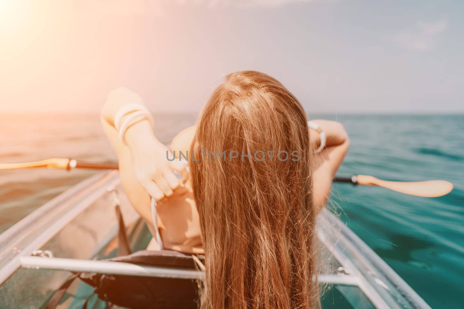 Woman in kayak back view. Happy young woman with long hair floating in transparent kayak on the crystal clear sea. Summer holiday vacation and cheerful female people having fun on the boat.