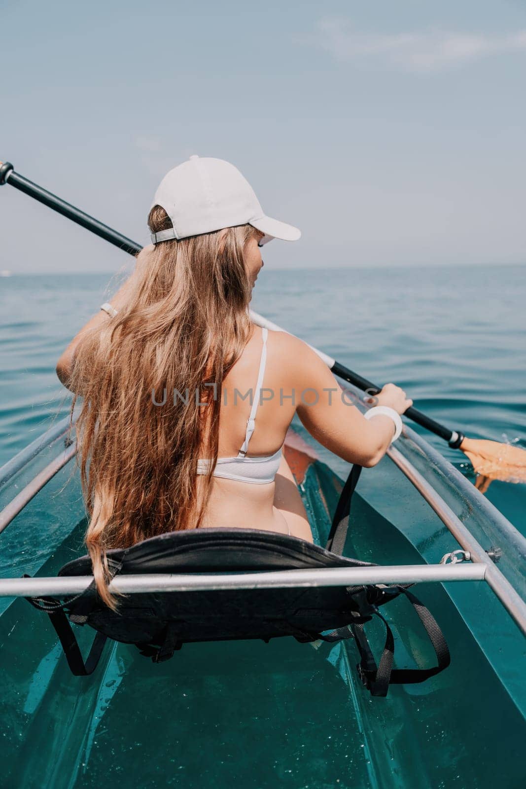 Woman in kayak back view. Happy young woman with long hair floating in transparent kayak on the crystal clear sea. Summer holiday vacation and cheerful female people relaxing having fun on the boat by panophotograph