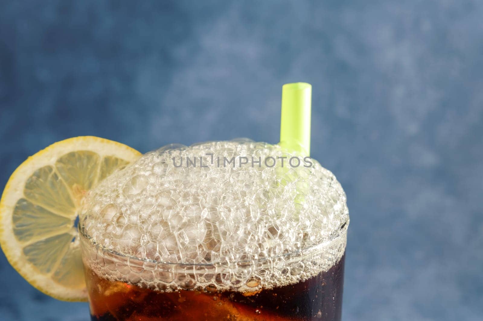 cola with ice and lemon with foam spilling out of the crystal glass