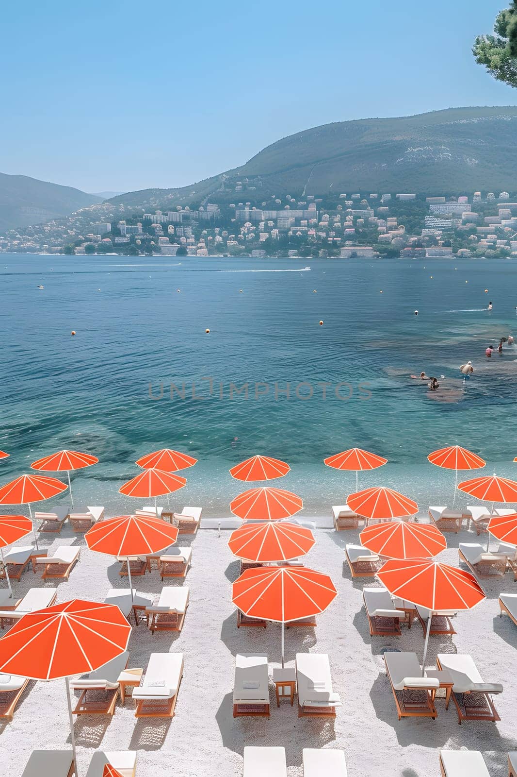 A stunning beach with numerous orange umbrellas and chairs, set against a backdrop of crystal clear water, blue skies, and majestic mountains. Perfect for leisure and relaxation