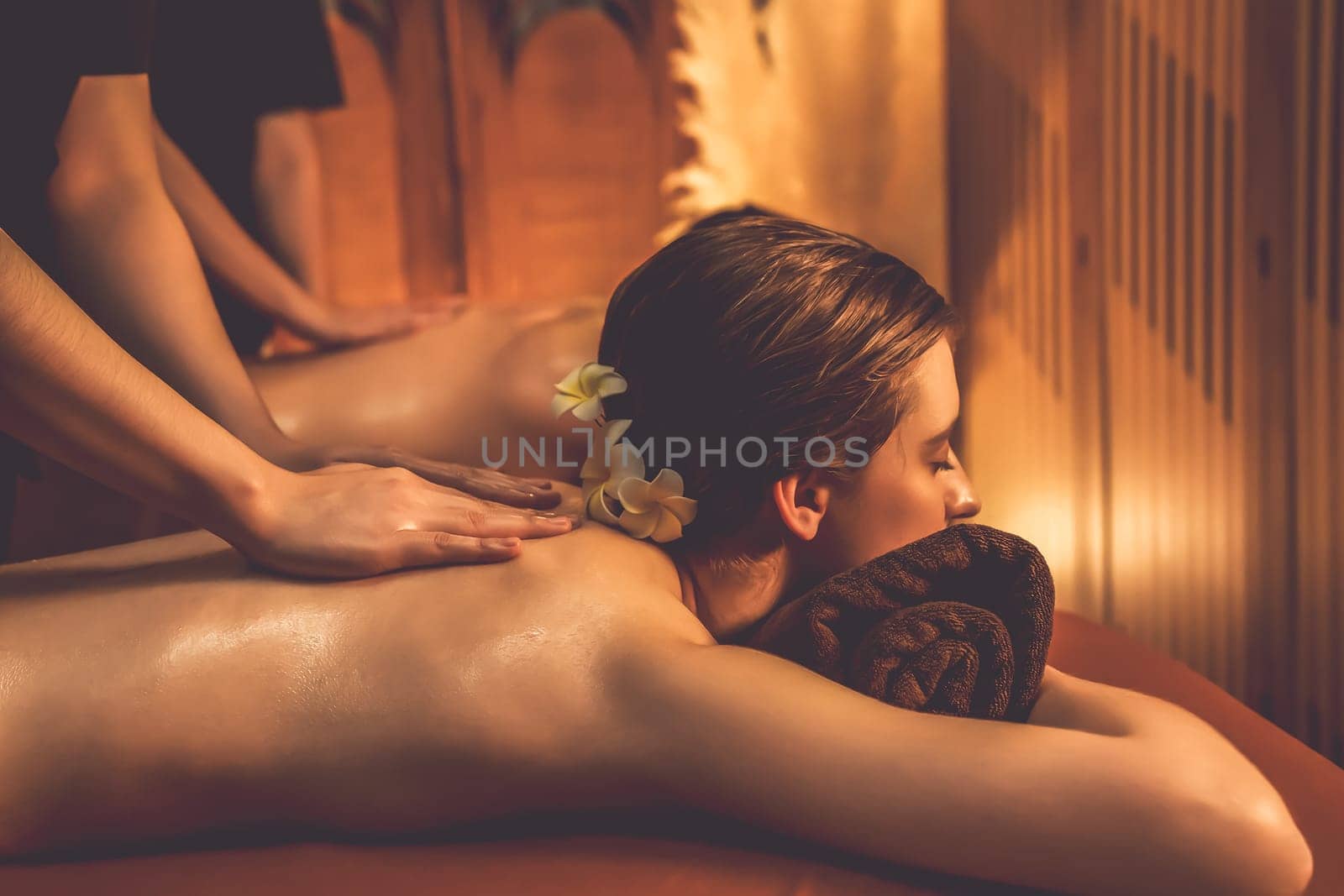 Caucasian couple customer enjoying relaxing anti-stress spa massage and pampering with beauty skin recreation leisure in warm candle lighting ambient salon spa at luxury resort or hotel. Quiescent