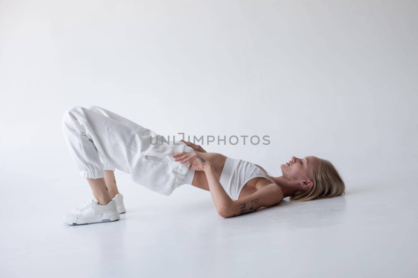 Beautiful blonde girl in a white top and tights posing on a white background. Lying on the floor. by Freeman_Studio