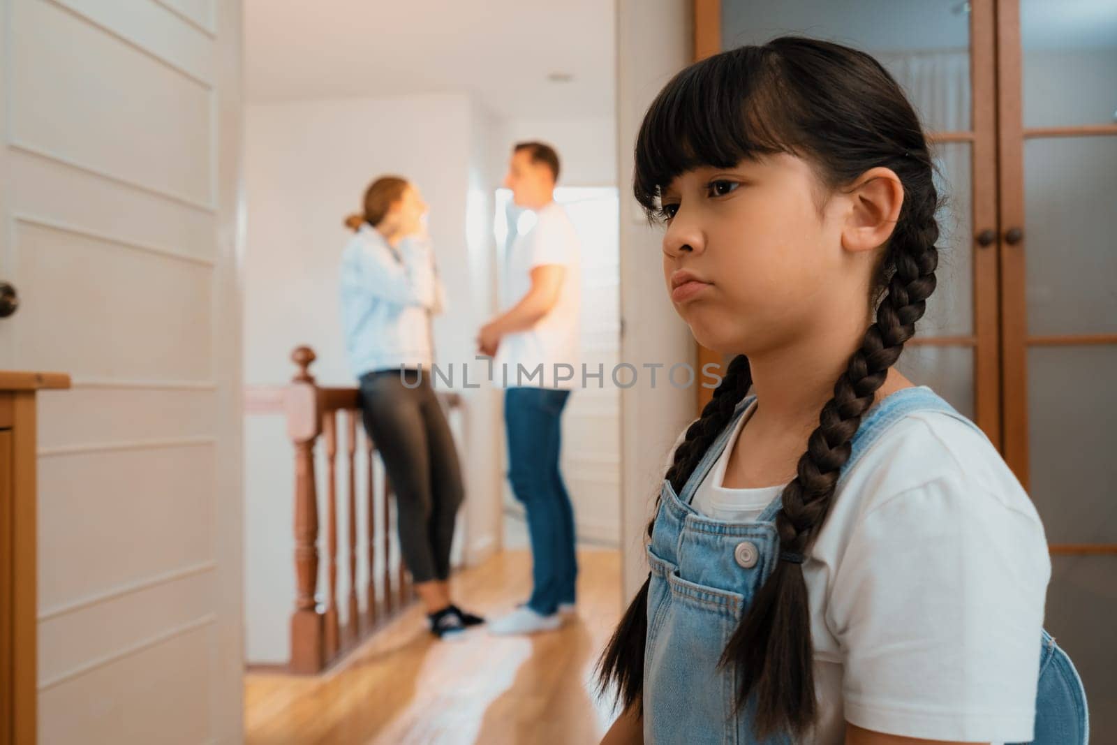 Stressed and unhappy young girl huddle in corner crying and sad while her parent arguing in background. Domestic violence at home and traumatic childhood develop to depression. Synchronos