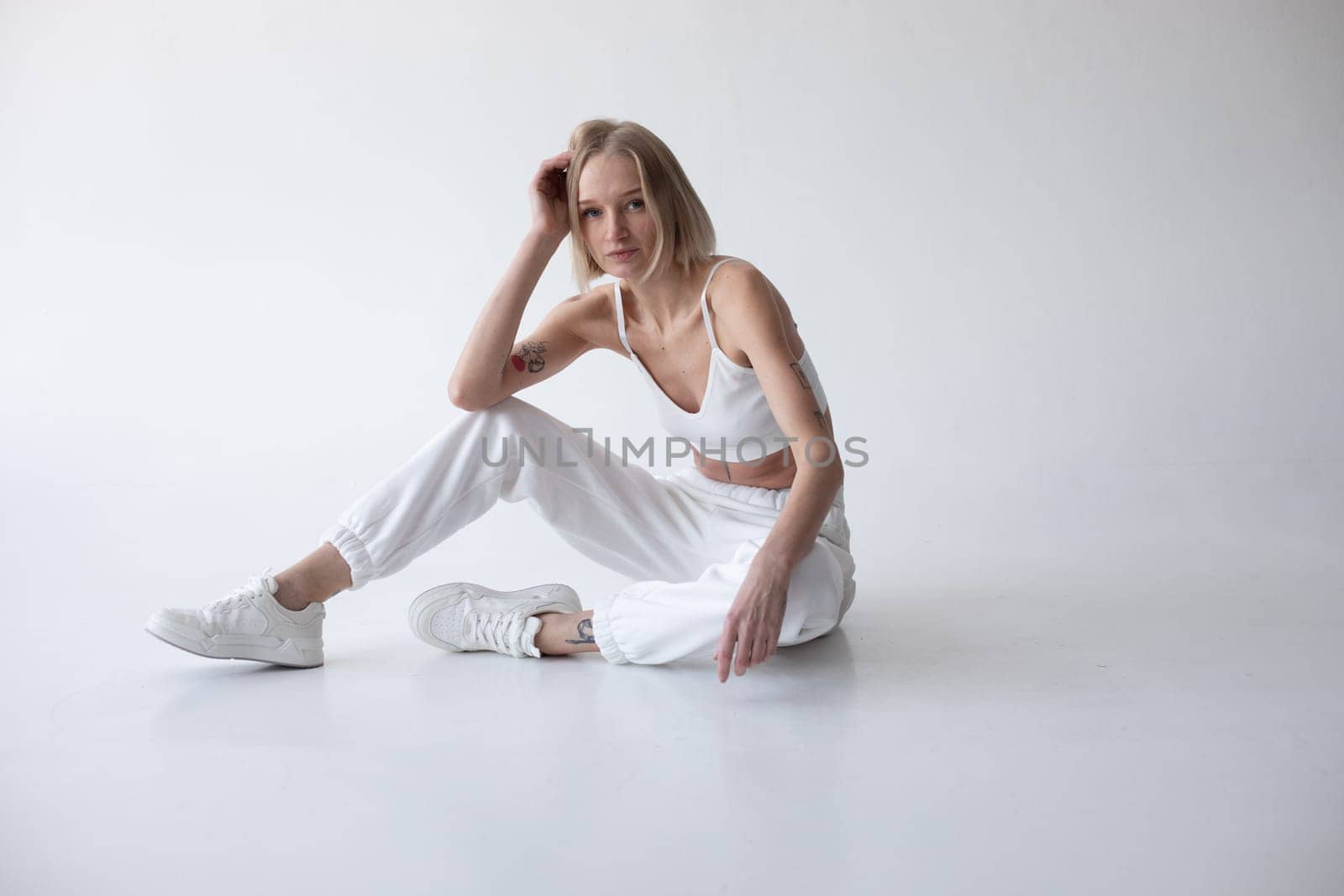 Beautiful blonde girl in a white top and tights posing on a white background. High quality photo