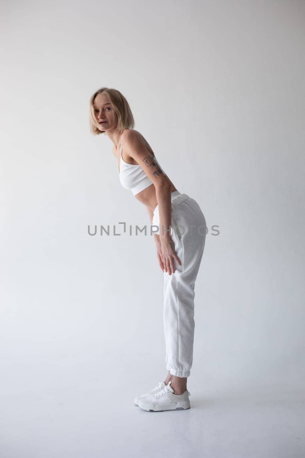 Beautiful blonde girl in a white top and tights posing on a white background. High quality photo