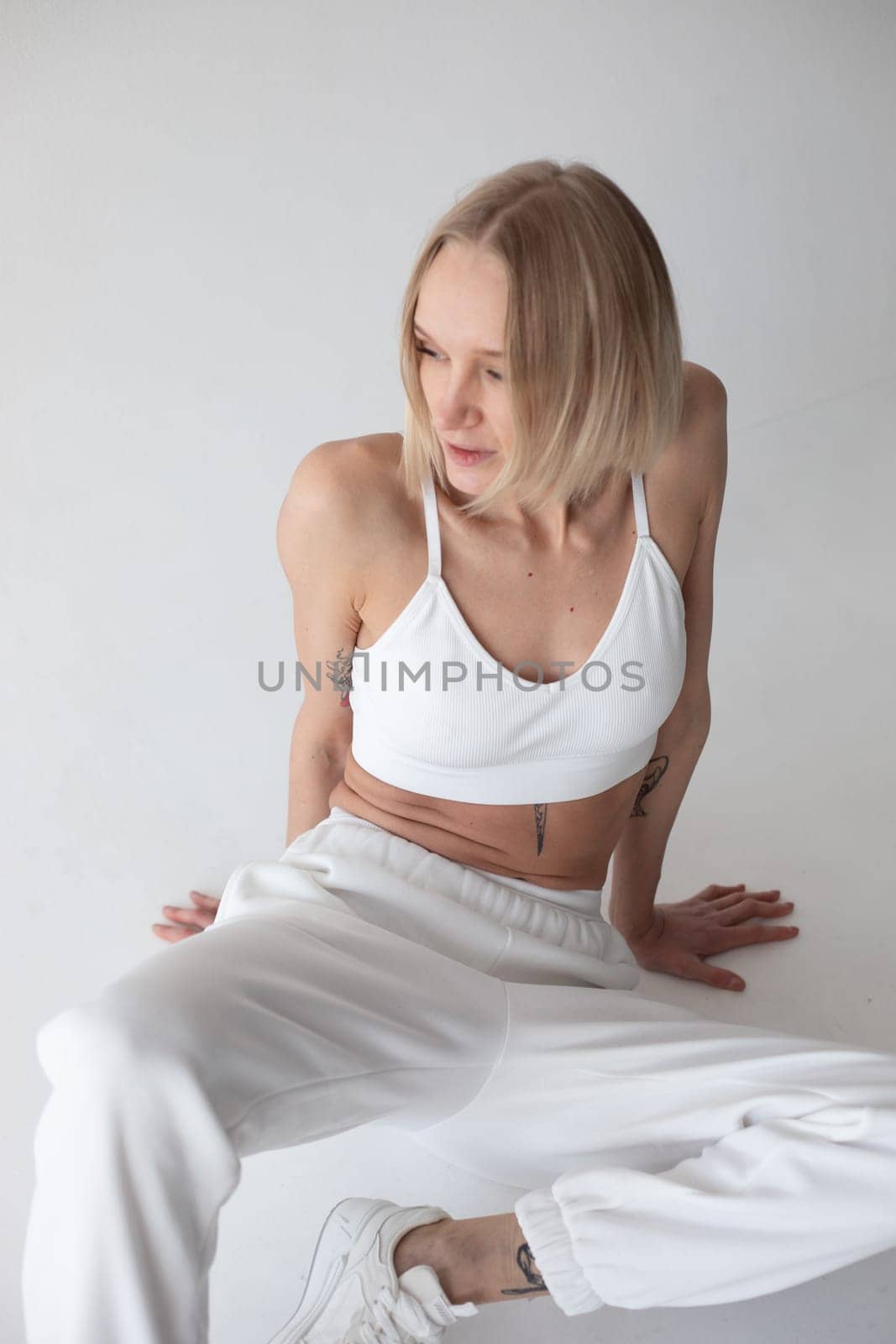 Beautiful blonde girl in a white top and tights posing on a white background by Freeman_Studio