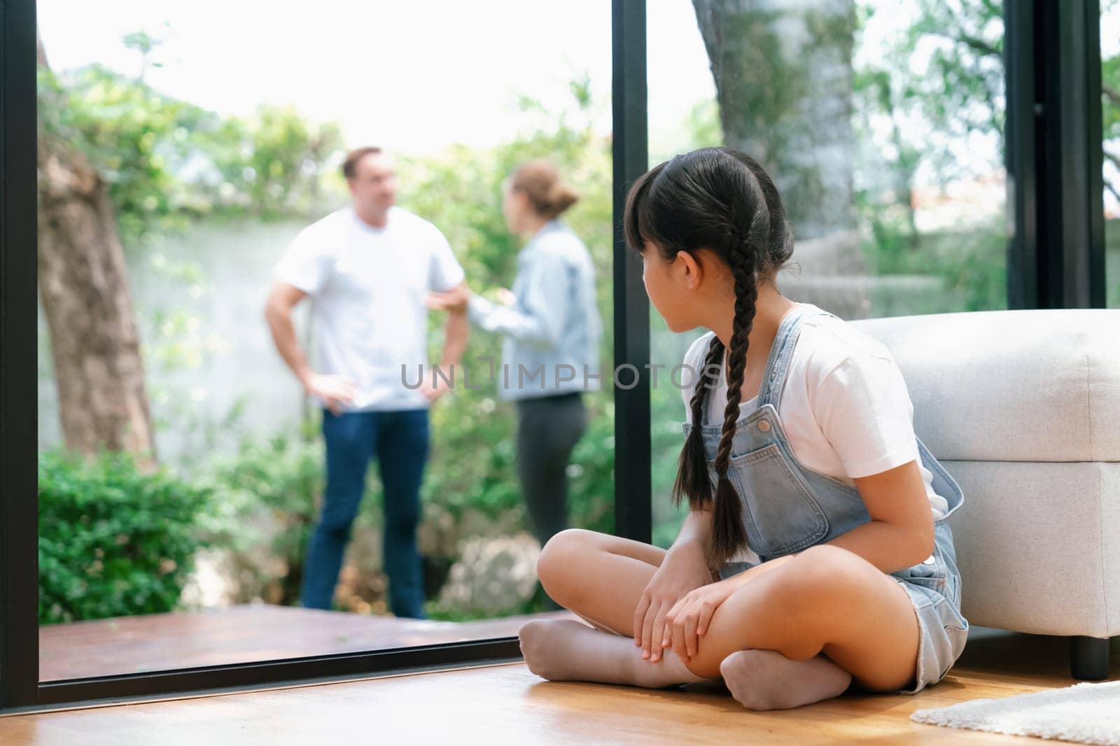 Stressed and unhappy young girl huddle in corner crying and sad while her parent arguing in background. Domestic violence at home and traumatic childhood develop to depression. Synchronos