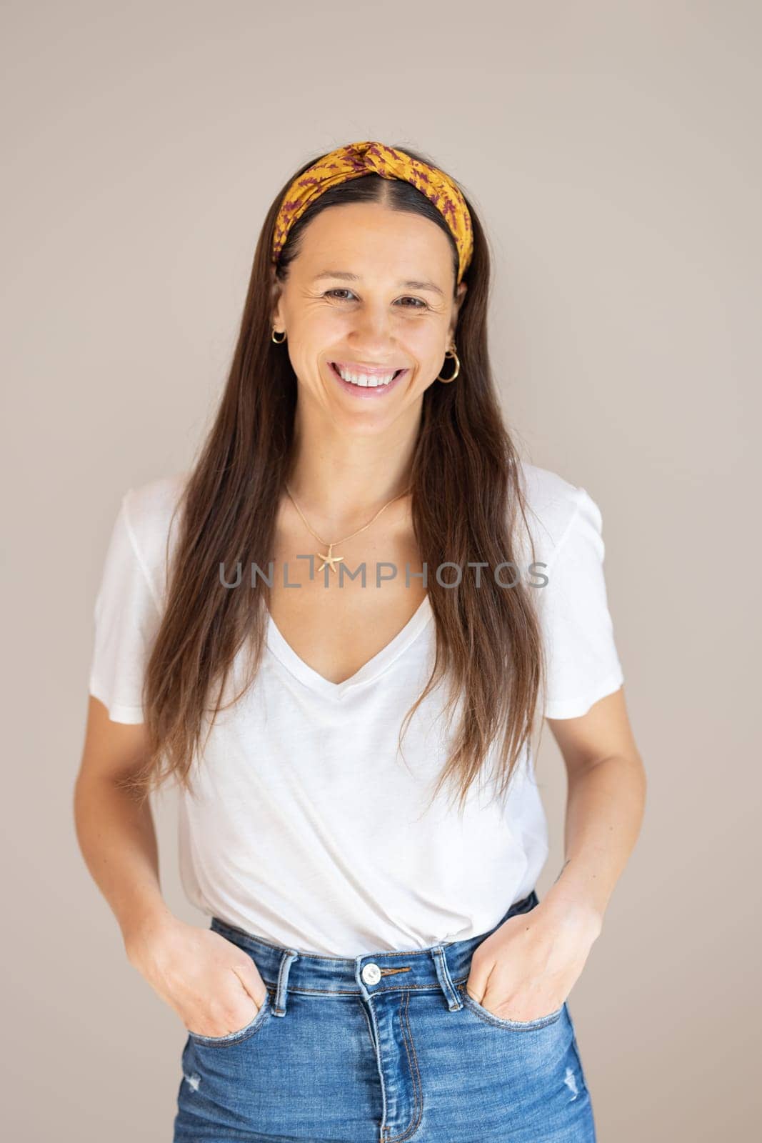 Portrait of confident beautiful woman with long brown hair, wearing casual clothes, standing in relaxed pose with hands in pockets, smiling with white teeth at camera, studio background. by kasto