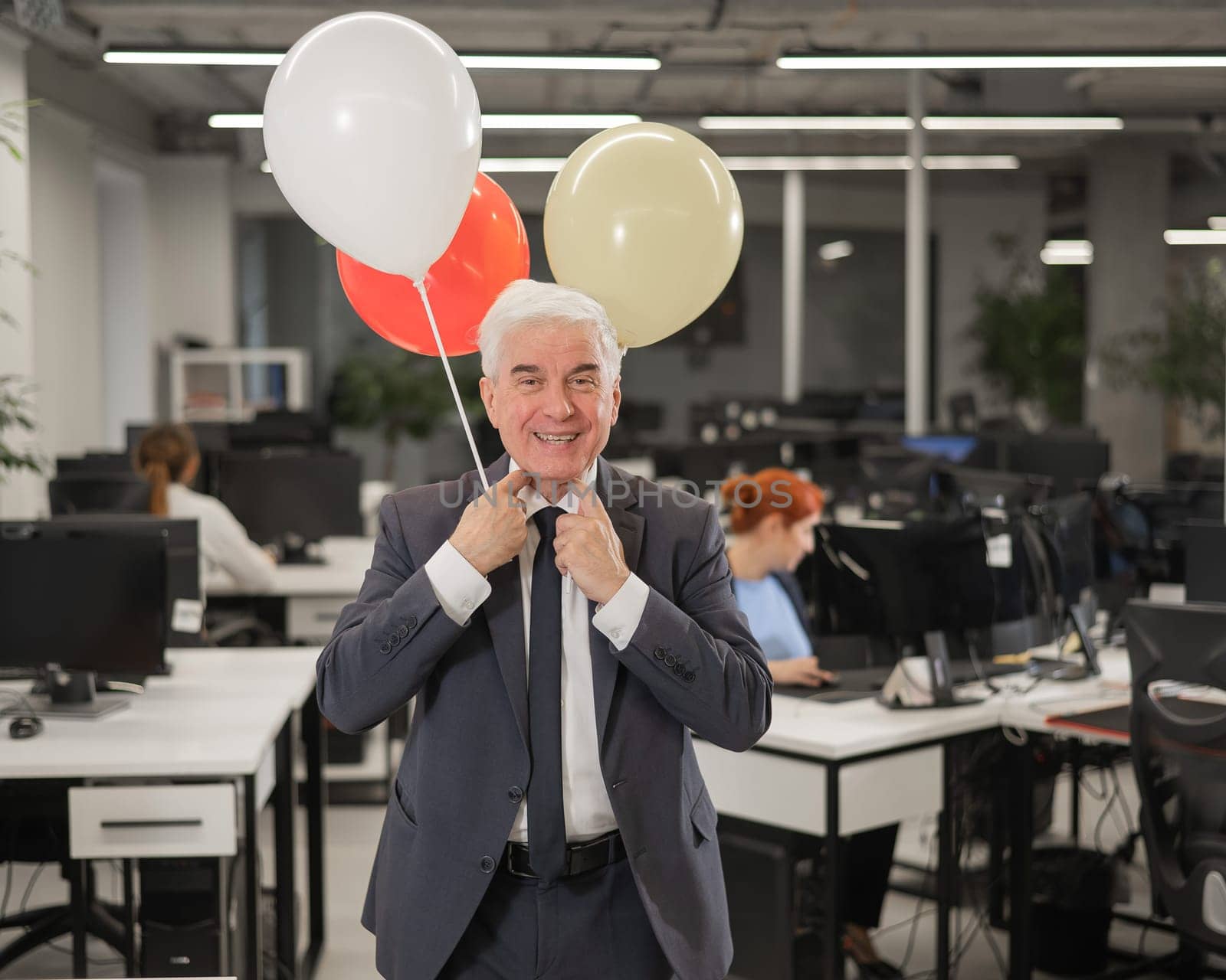 Portrait of a cheerful mature business man holding balloons in the office