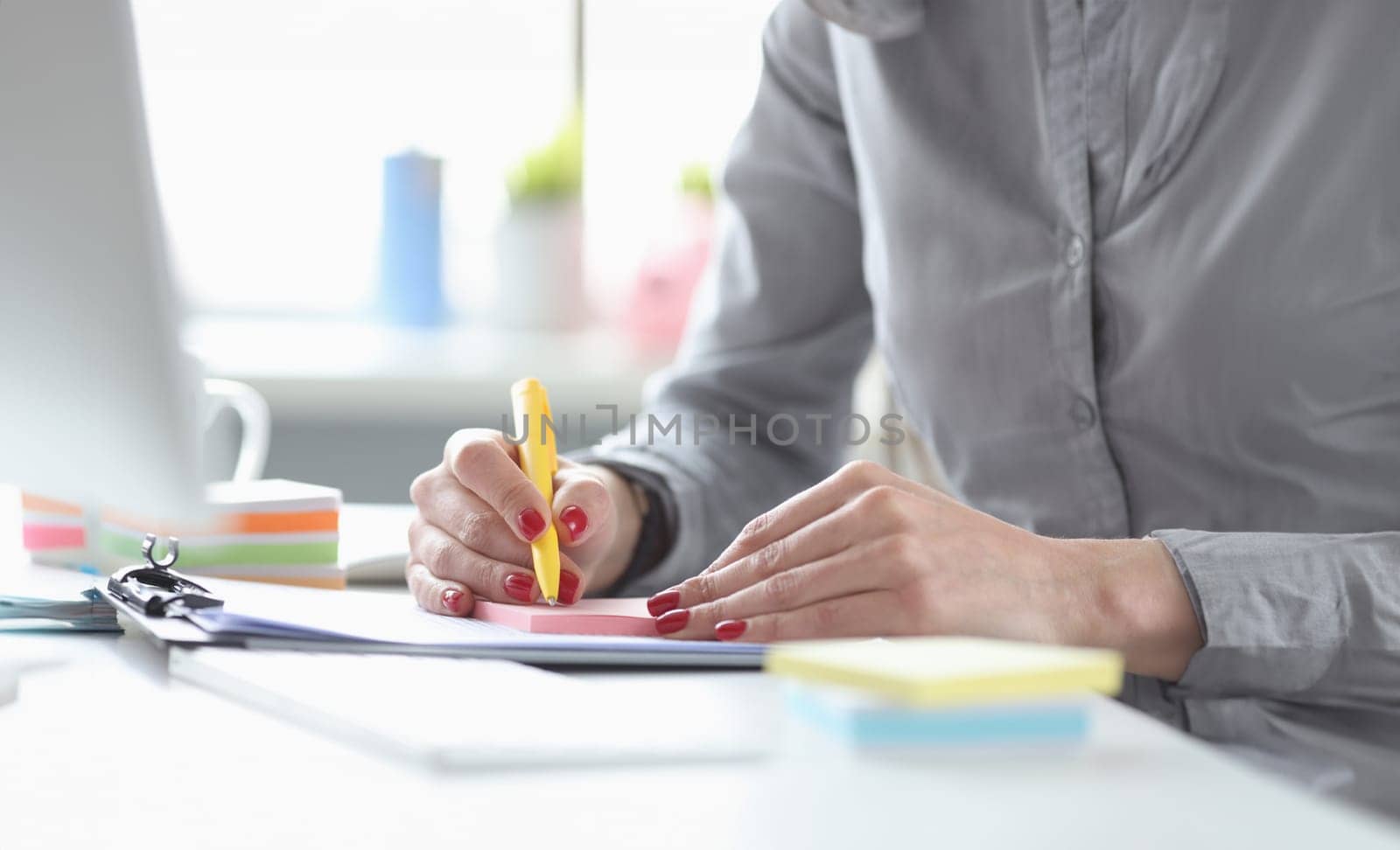 Business woman with red manicure writing with pen on paper stickers closeup. Secretary work concept
