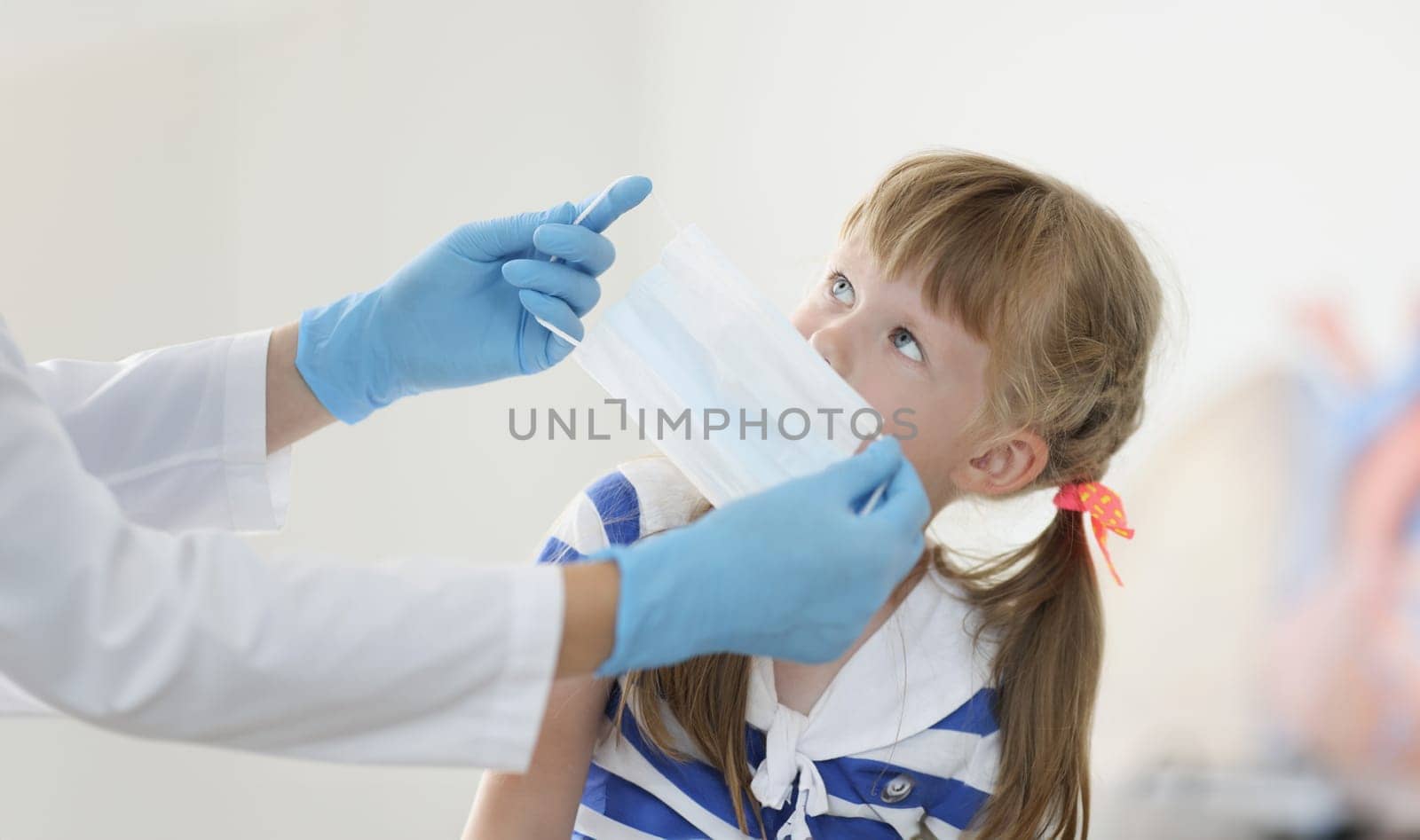 Doctor putting protective medical mask on little girl in clinic. Prevention covid19 mask mode concept