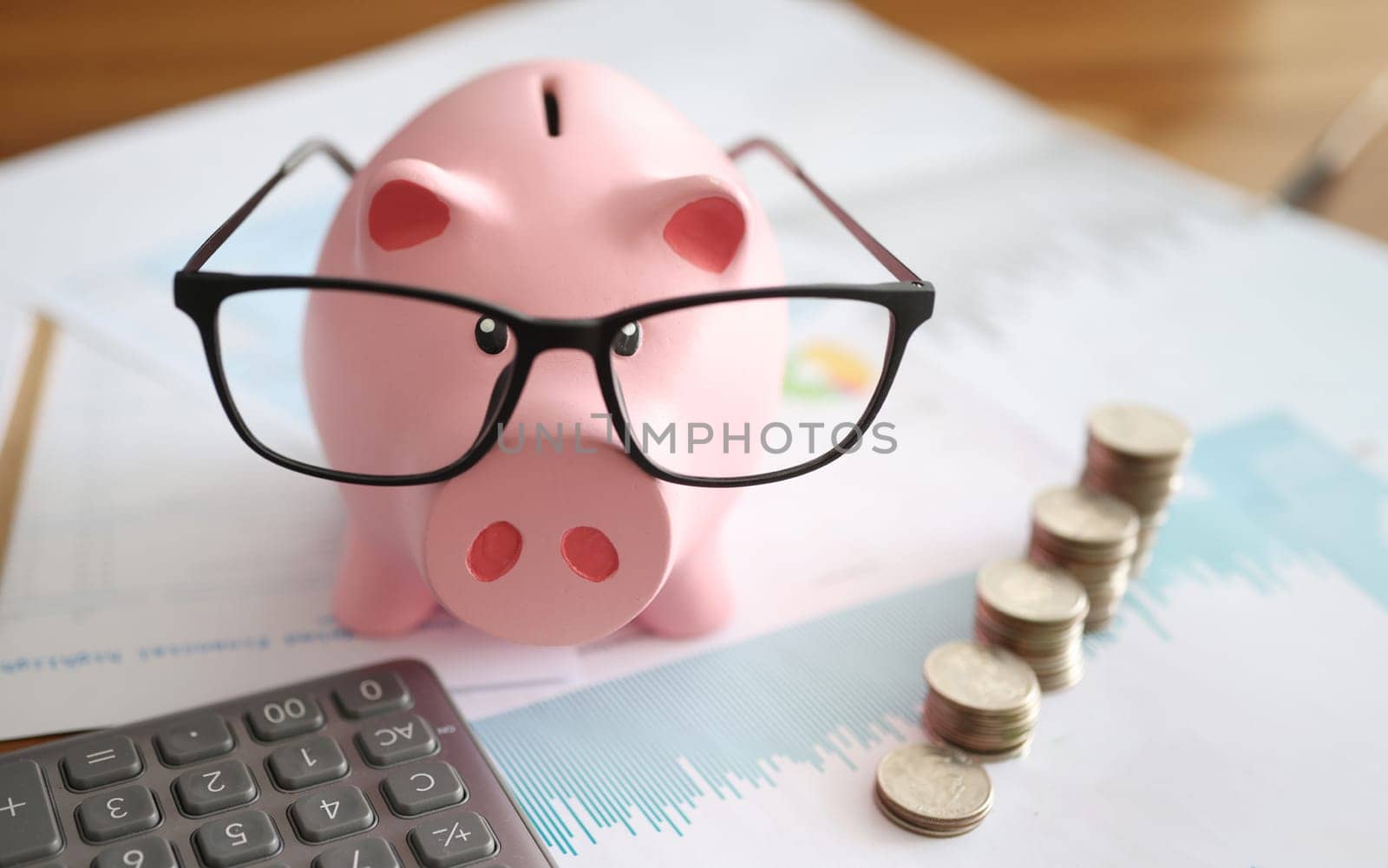 Pink piggy bank with glasses standing near heaps of coins and calculator closeup by kuprevich