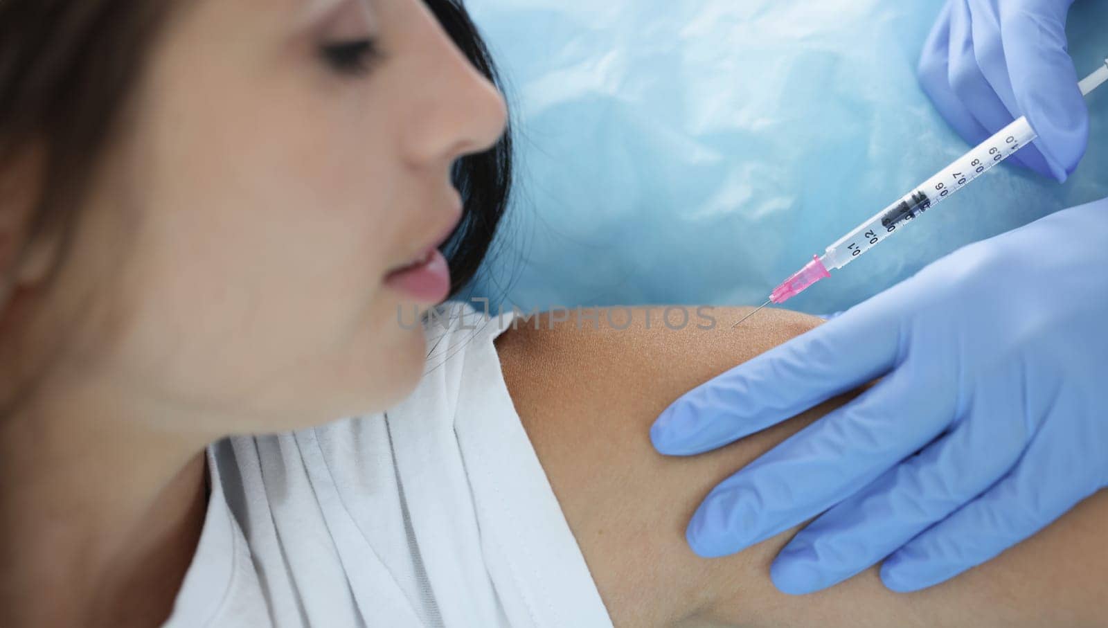 Nurse giving injection in shoulder of young woman in clinic closeup. Vaccination against covid 19 concept
