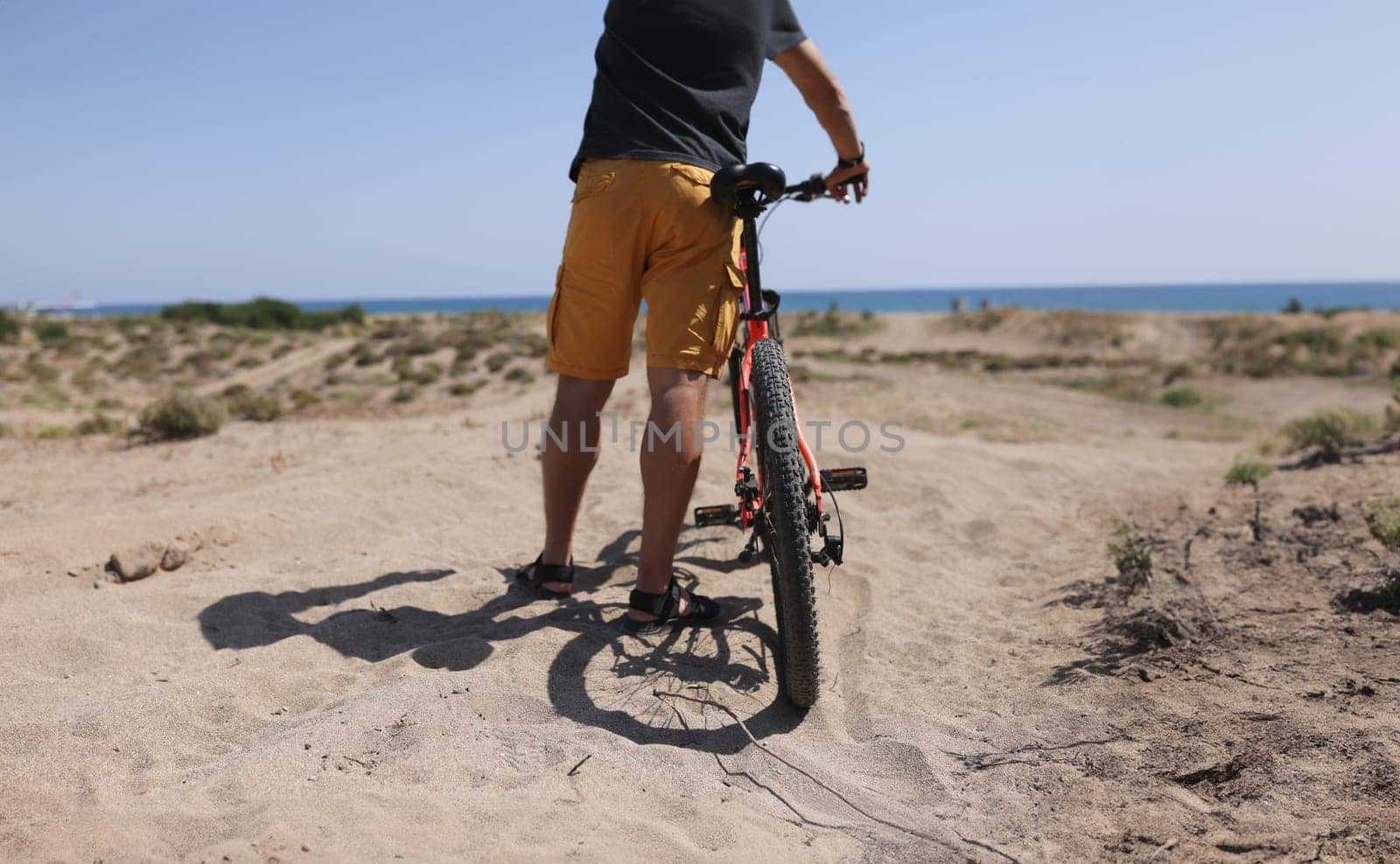 Man holding bike on sand near sea closeup by kuprevich
