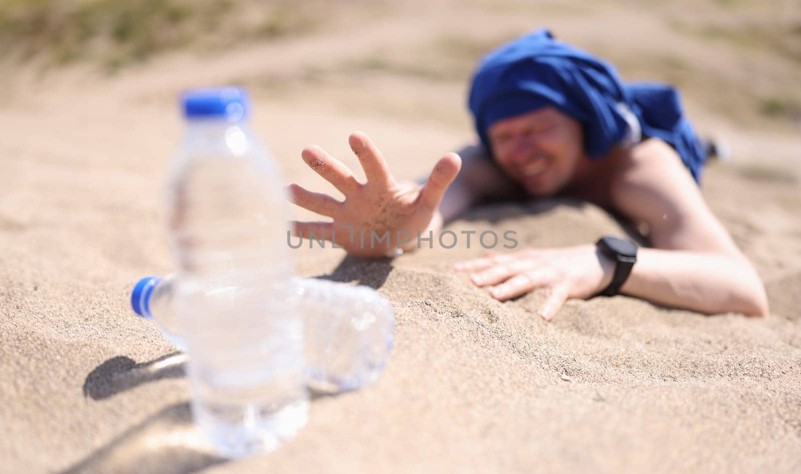 Dehydrated man crawling on sand for bottle of drinking water closeup by kuprevich