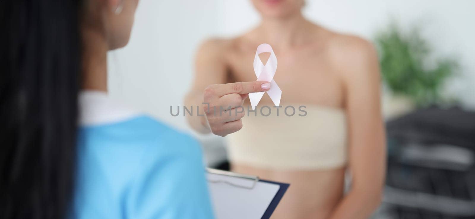 Woman with bandaged chest holding pink ribbon at doctor appointment closeup by kuprevich