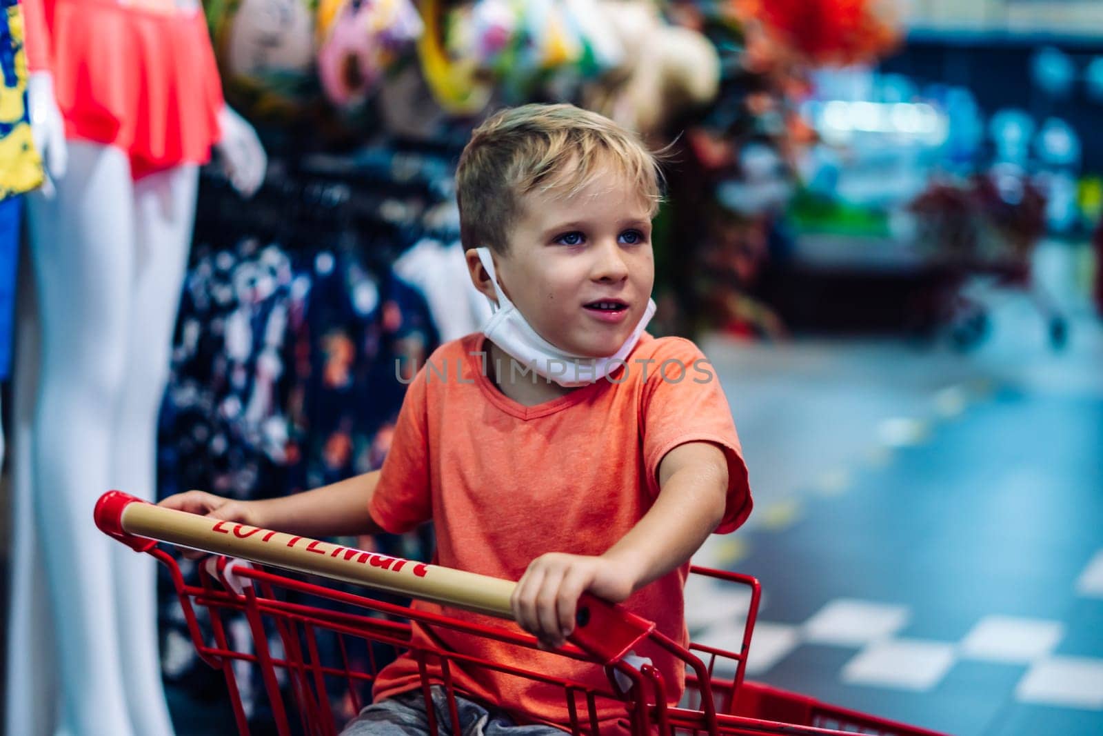 Boy sitting in shopping cart clothing store hypermarket, interested curious emotion, happy childhood.