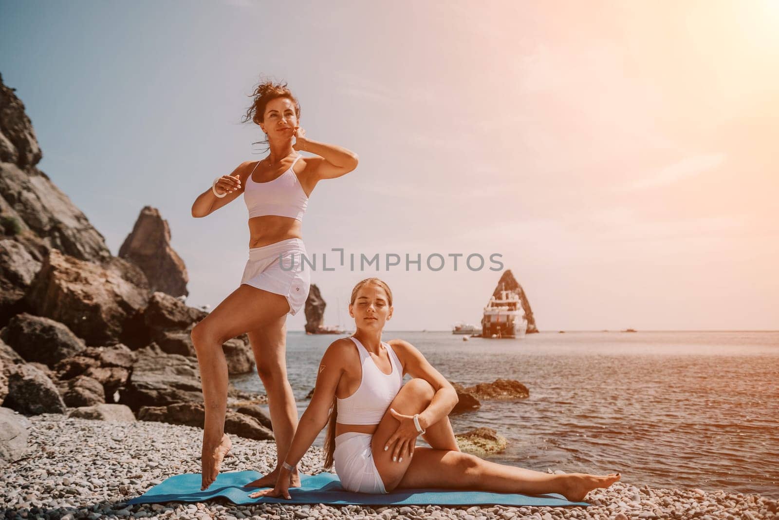 Woman sea yoga. Two happy women practicing yoga on the beach with ocean and rock mountains. Motivation and inspirational fit and exercising. Healthy lifestyle outdoors in nature, fitness concept. by panophotograph