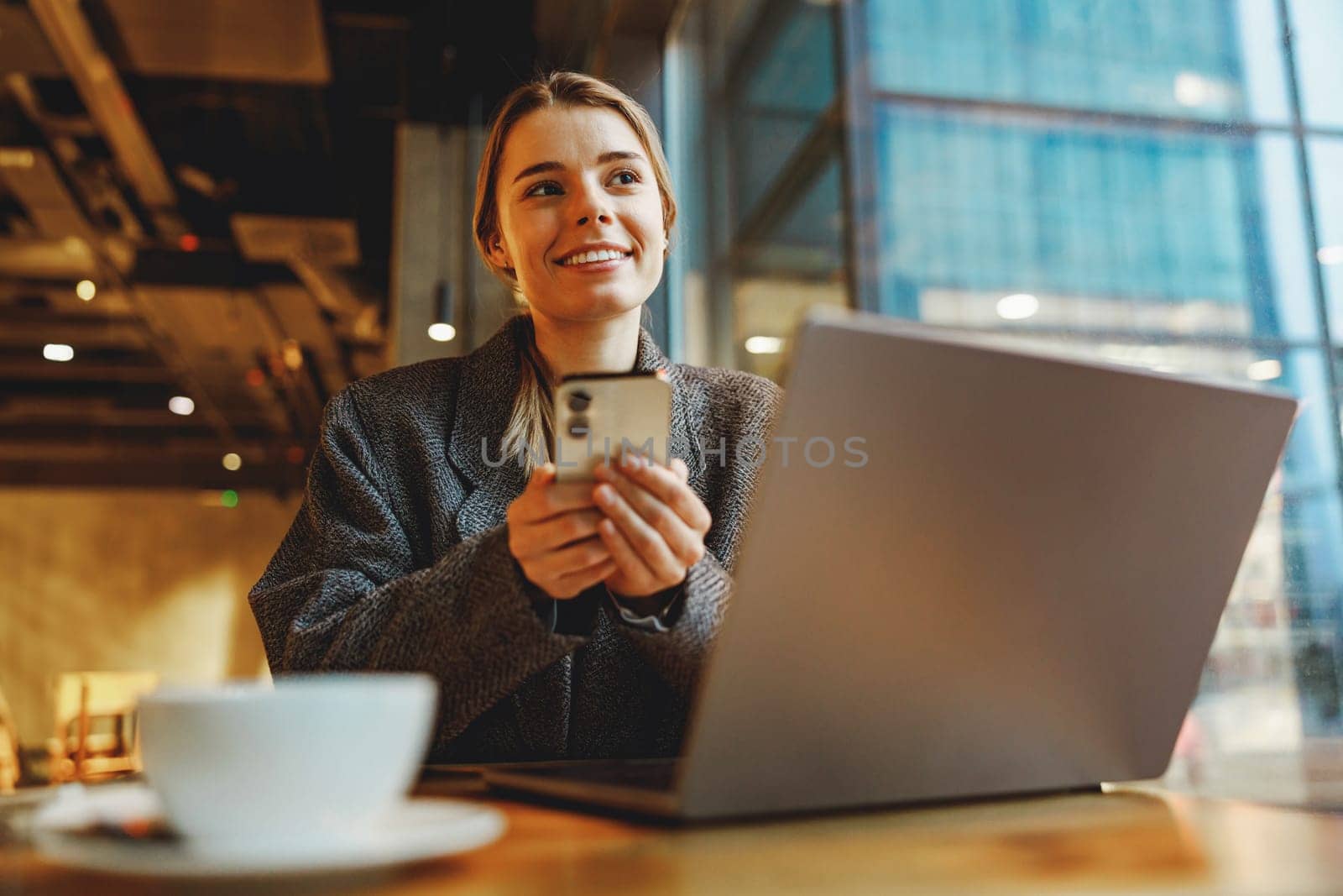 Woman manager reading message on phone and work on laptop in cafe. Distance work concept