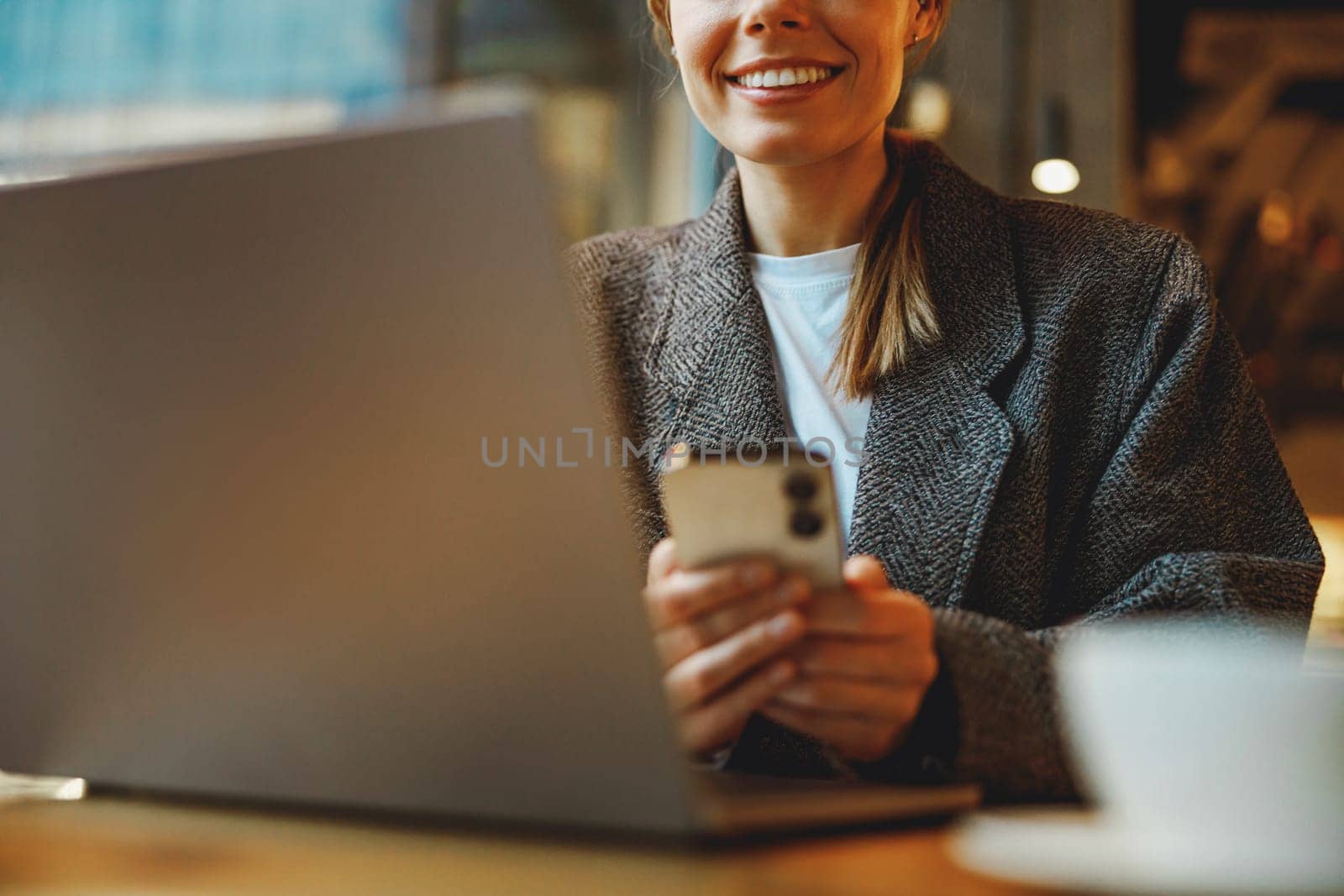 Smiling woman manager is using phone and work on laptop outside of office. Distance work concept